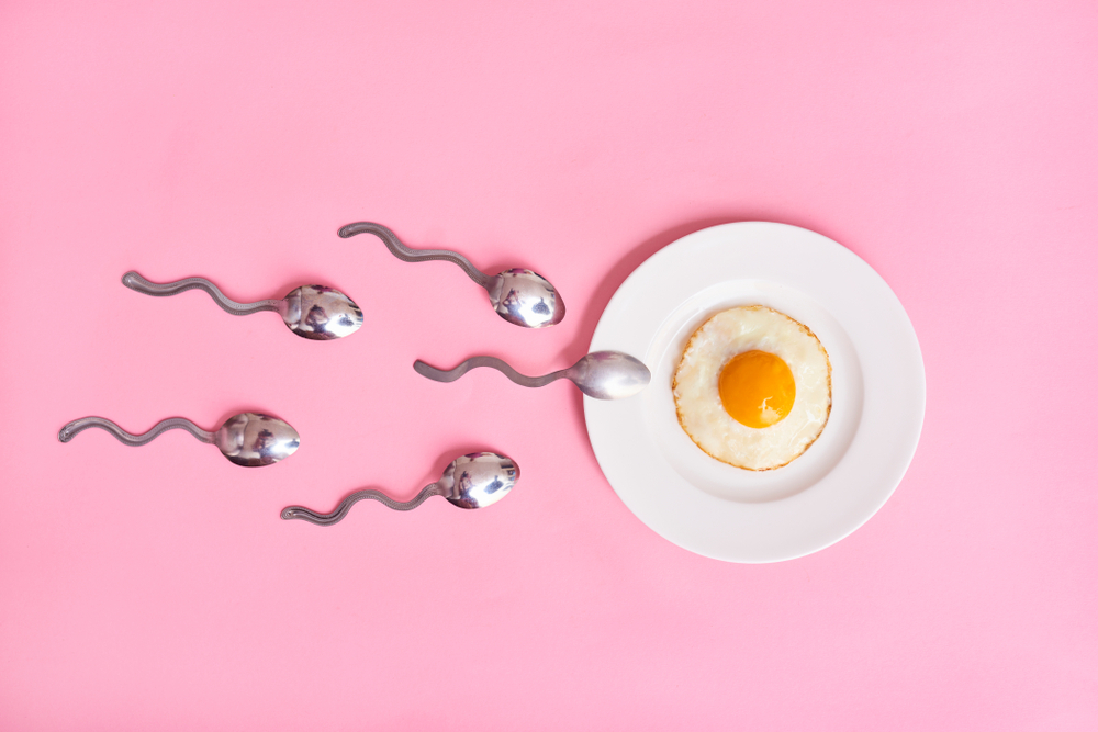Sppons in the shape of sperm swimming towards a fried egg on a plate