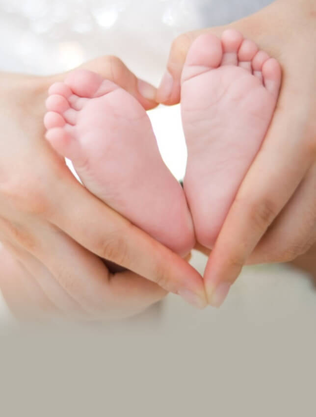 Baby's tiny feet cupped by mumma's hand forming a heart